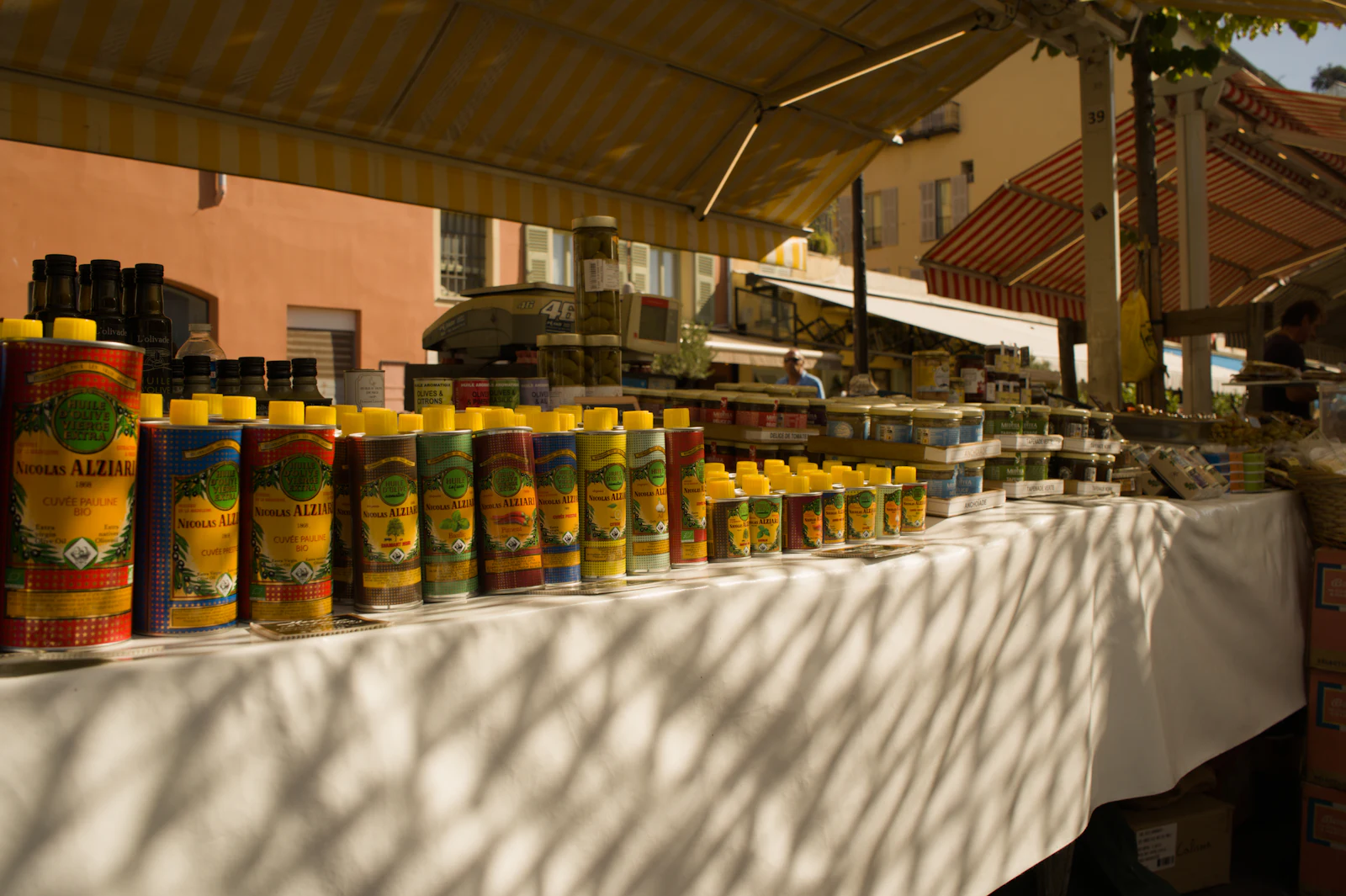 Olivenöldosen und -flaschen aufgereiht an einem Marktstand in der Sonne